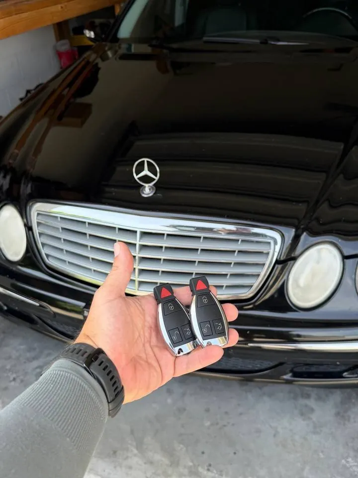 Two new Mercedes-Benz smart keys held in front of the customer's car